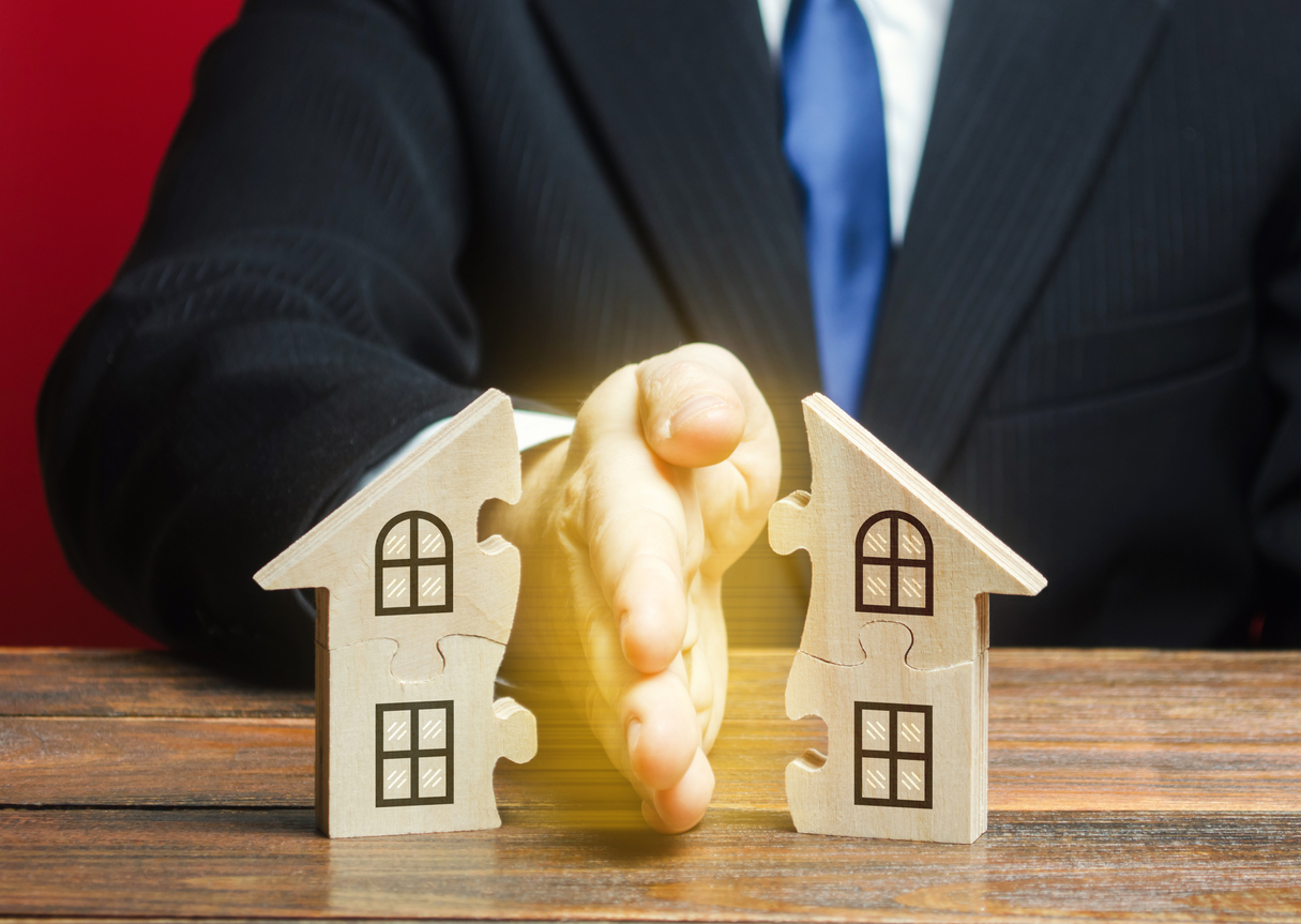 lawyer with hand slicing a wooden cutout of a home in half to symbolize property division in divorces